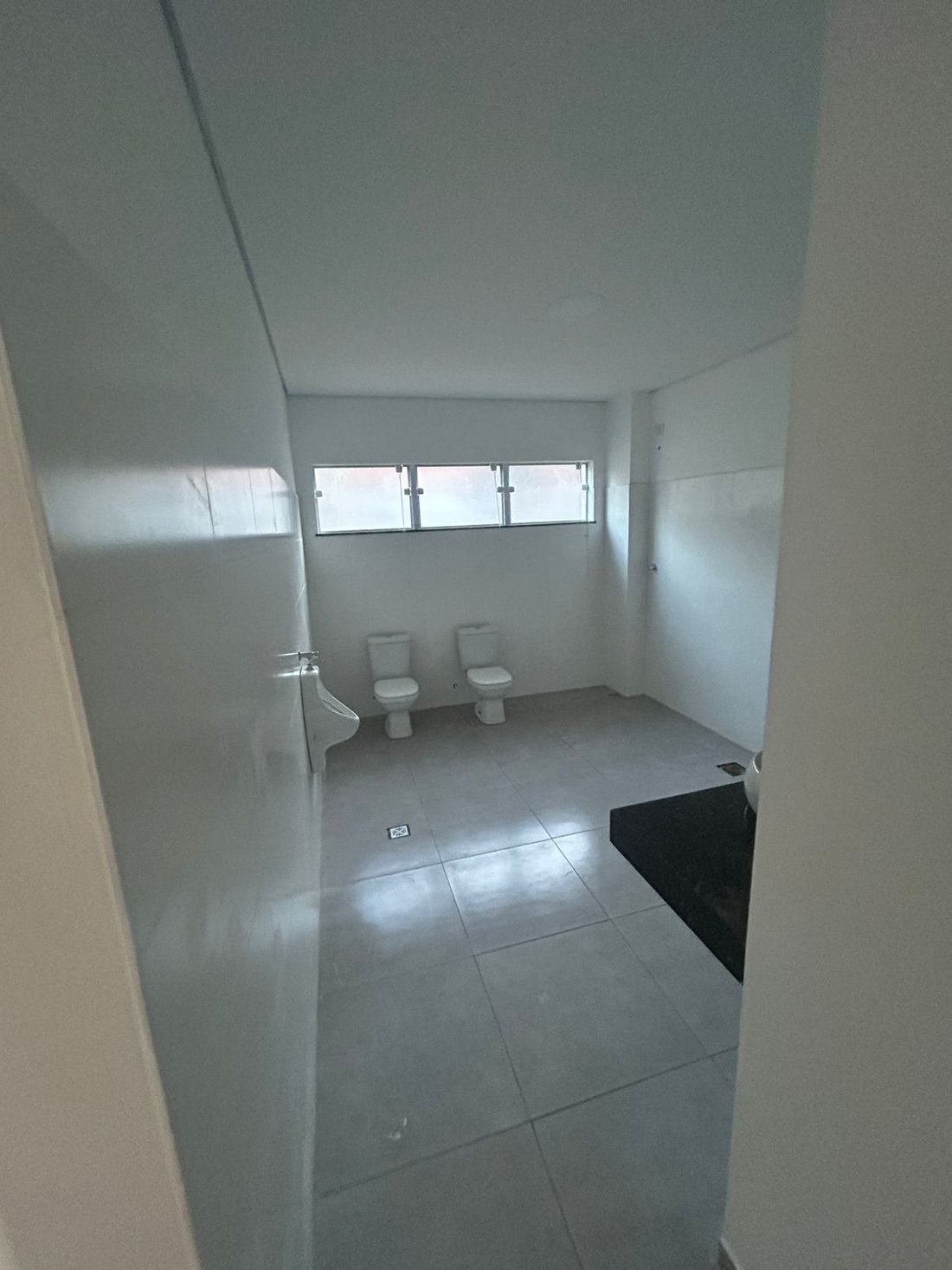 Banheiro coletivo com bacias sanitárias e mictório