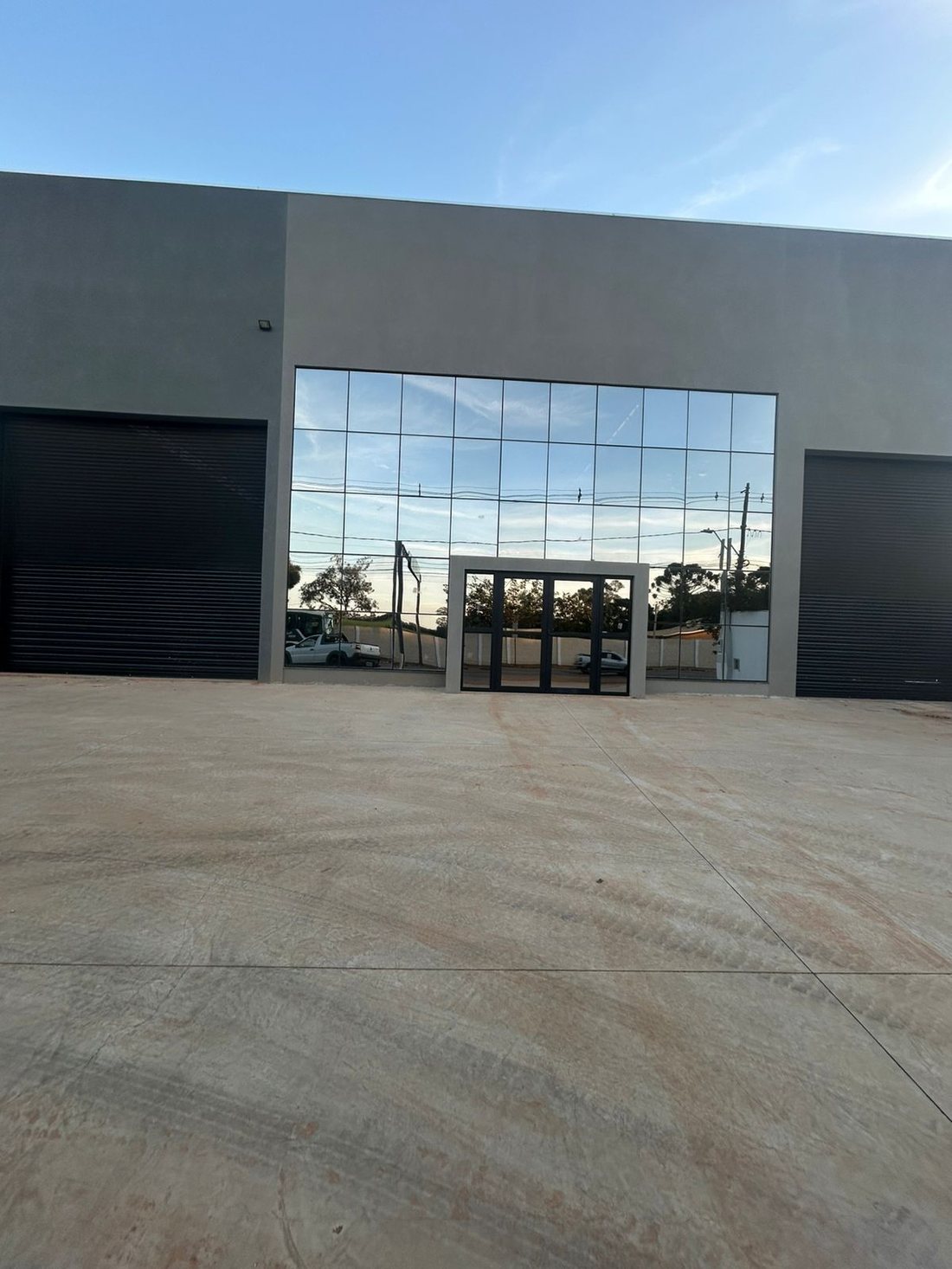 Detalhe da entrada de um galpão, com porta de vidro e portões de carga pretos