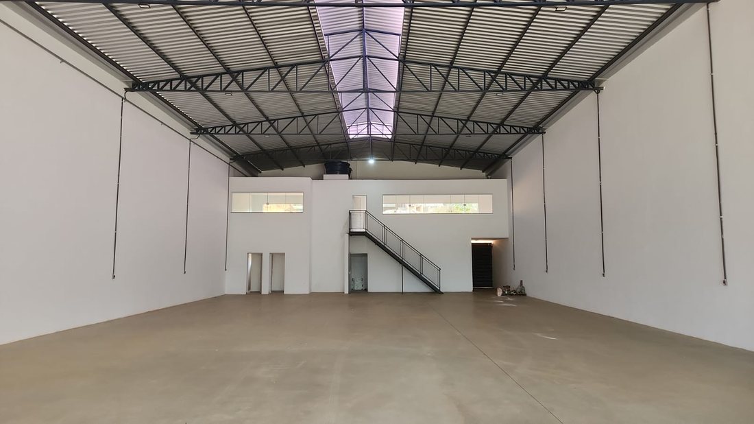 Interior do galpão vazio, mostrando mezanino, escada e portão de carga ao fundo